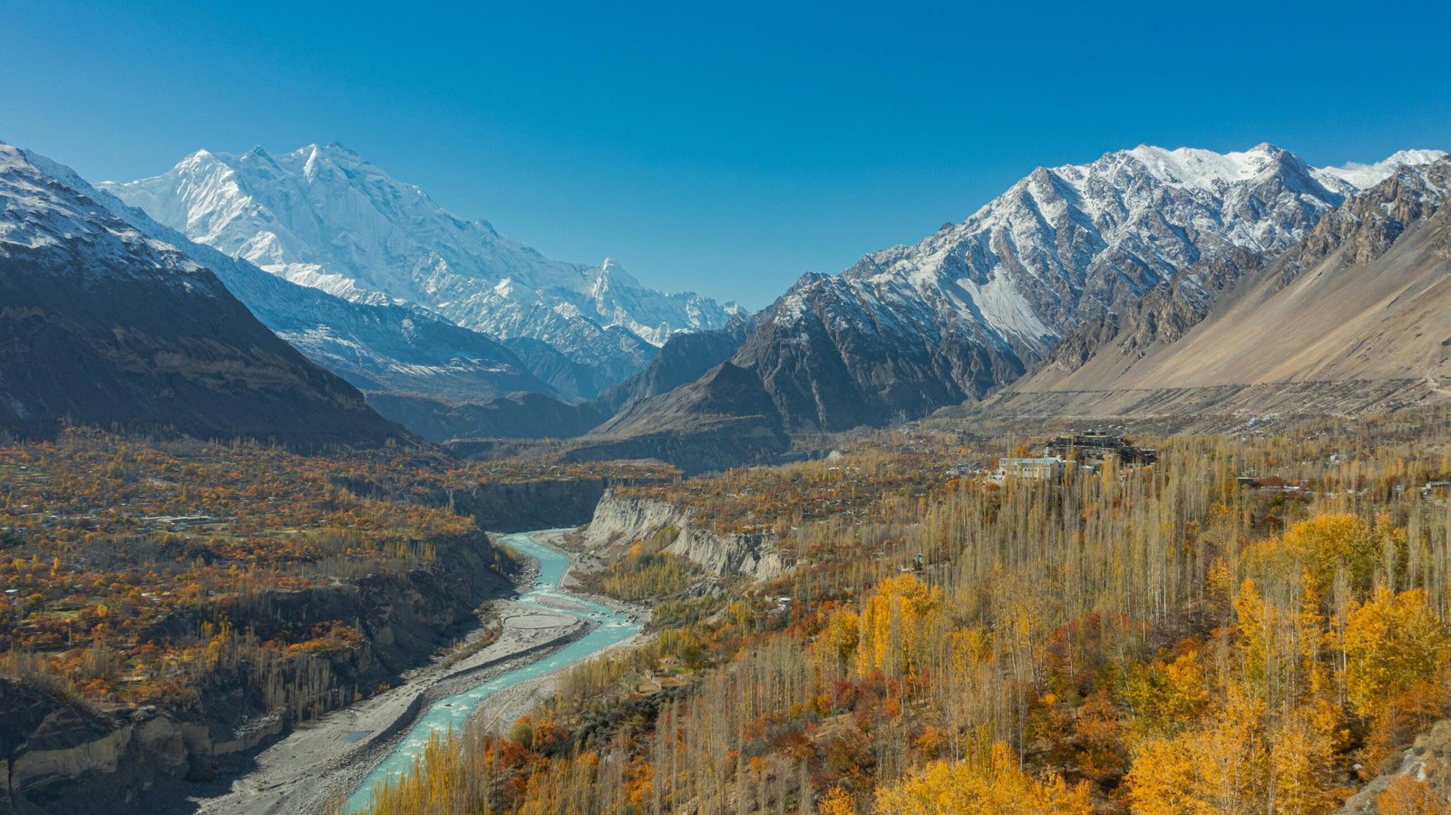 Stunning aerial view of Hunza Valley in autumn with snow-capped mountains and a winding river.